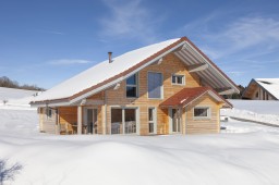 Chalet traditionnel en madriers dans un paysage enneigé de Franche-Comté.